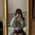Person taking a mirror selfie in a large gold ornate frame, wearing a gray hoodie and ripped black jeans, face obscured by phone